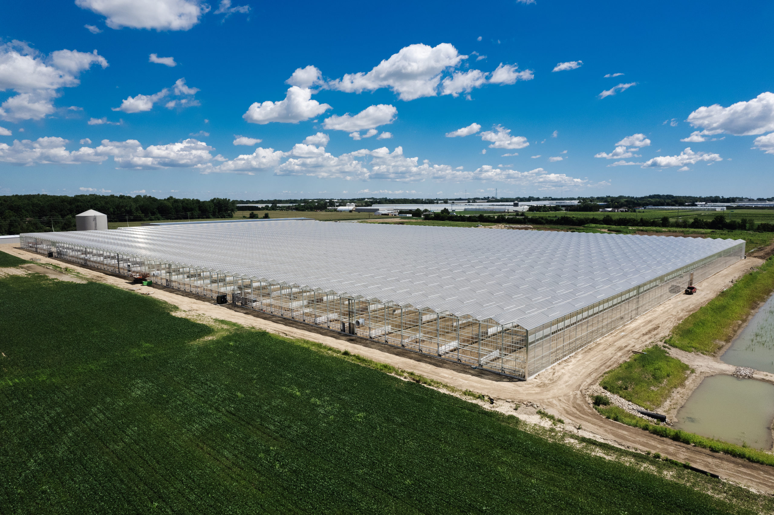 a bird's eyes view of an A Frame greenhouse in construction in the middle of a farming land under the bright sky